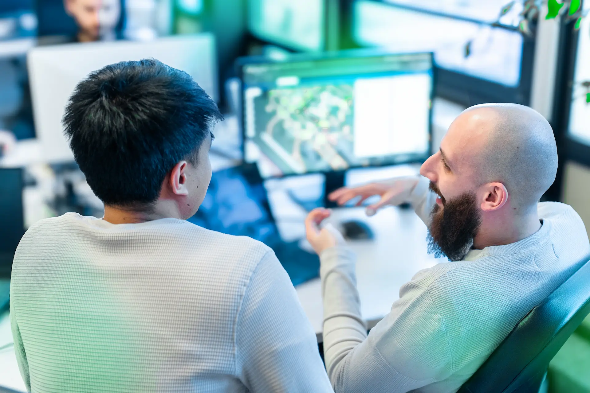 Due colleghi seduti a una scrivania in ufficio discutono animatamente di un progetto software, con un monitor in primo piano che mostra un’interfaccia di sviluppo.